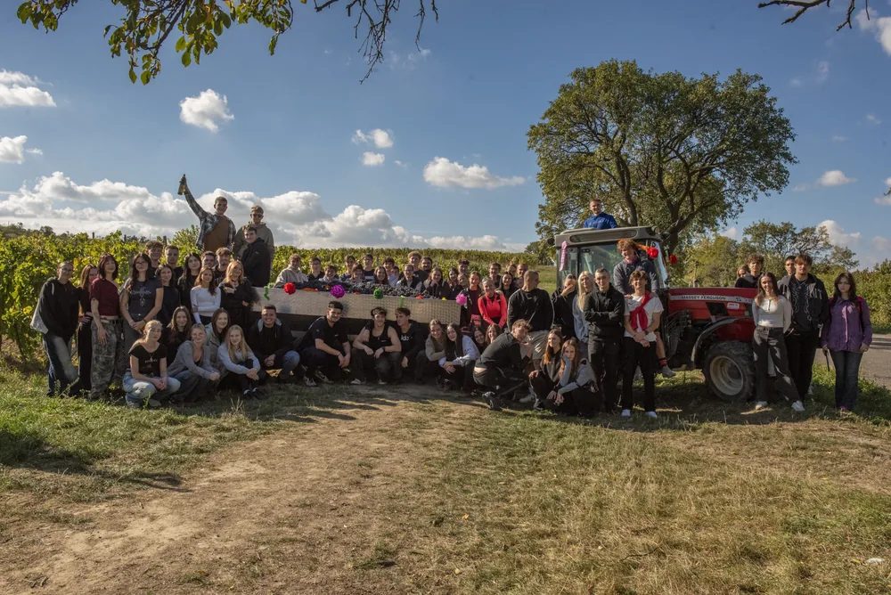Společná fotografie studentů u vinice se školním traktorem